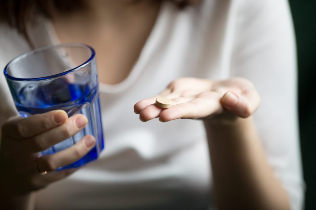 female hands holding pill and glass of water, closeup view