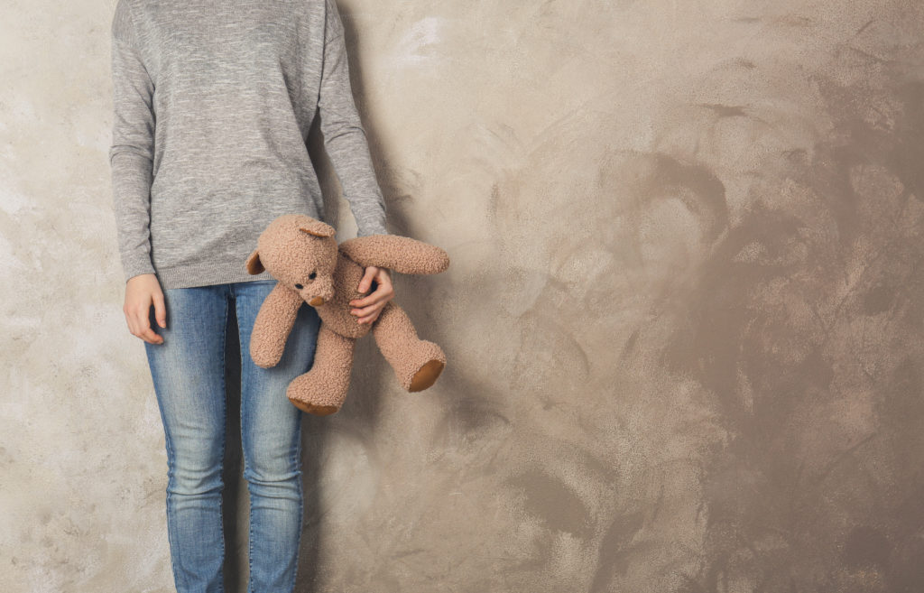 little girl standing with toy bear on color wall background
