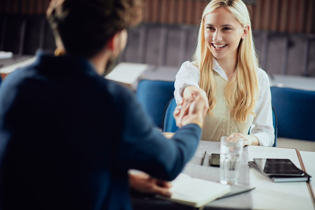 two business partners shaking hands while sitting in coffee shop
